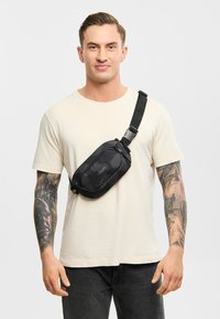 Geantă neagră tip crossbody, fabricată dintr-un material durabil, cu o textură netedă și un design curbat. Dispune de o curea ajustabilă și detalii subtile cu logo.