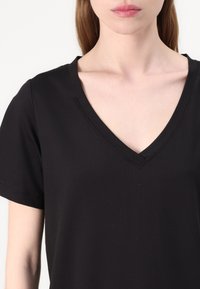 Black V-neck t-shirt with short sleeves, made of smooth fabric. Features a minimalistic design and subtle stitching along the neckline.