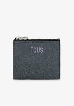 Billetera de cuero texturizado gris oscuro con cierre de cremallera. Logo "TOUS" grabado en gris más claro en la parte frontal. Forma rectangular compacta.
