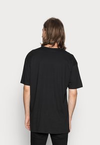 Camiseta negra de manga corta y escote redondo, que muestra un ajuste holgado. El material parece suave con una textura lisa.