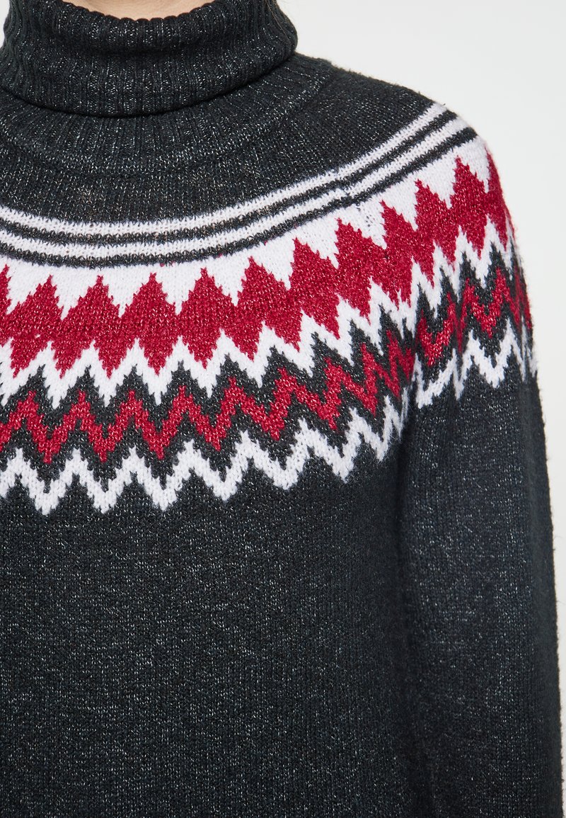 Dzianinowy sweter z golfem w ciemnoszarym kolorze z wzorzystą wstawką, która ma zygzakowate wzory w czerwonym, białym i czarnym kolorze. Miękka tekstura.