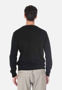Maglione nero a coste con maniche lunghe, scollatura a girocollo e orlo aderente, abbinato a pantaloni beige chiaro. Focus sulla texture e sul contrasto di colore.
