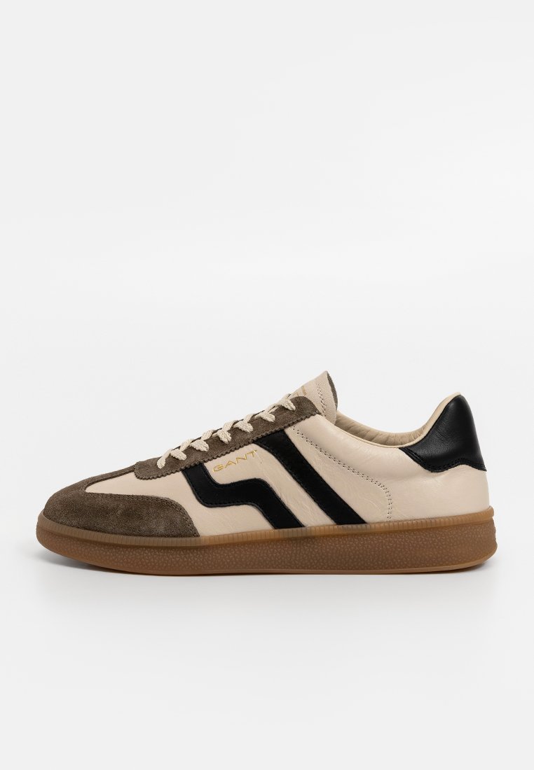 Męskie sneakersy z kremową skórzaną cholewką, brązowymi zamszowymi akcentami, czarnymi paskami i gumową podeszwą. Posiadają płaskie sznurówki i zaokrąglony czubek.