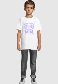 Bílý bavlněný tričko s grafikou fialového motýla a textem "DOBRÁ KARMA", doplněné šedými slim-fit džíny a šedými teniskami.