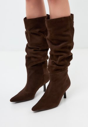 Bruine suède slouchy kniehoge laarzen met spitse neuzen en stilettohol. Zachte textuur met geplooide details rond de bovenkant.