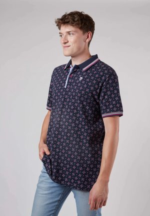 Polo shirt marine avec un motif floral rose et blanc, doté d'un col à boutons et d'accents rayés sur les manches. Tissu en mélange de coton doux.