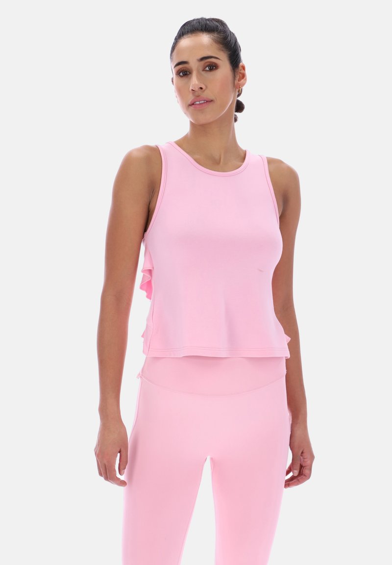 Joven mujer con top sin mangas color rosa claro y leggings a juego, posando frente a un fondo blanco liso.