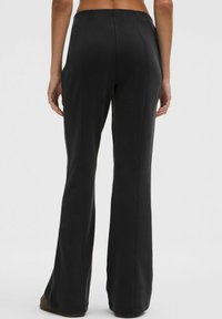 Čierne rozšírené nohavice s hladkou textúrou, obsahujúce viditeľné detaily švov a stredne vysoký pás. Pohľad zozadu ukazuje priliehavý strih.