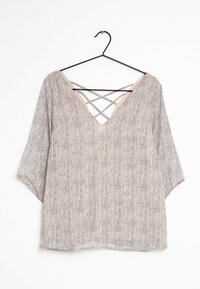 Blusa leggera e strutturata con scollatura a V e dettagli incrociati sul retro. Presenta una palette di colori neutri con un motivo delicato.