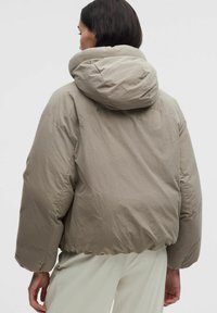 Padded béžová bunda s kapucňou, vyrobená z hladkého materiálu a s kratším strihom. Obsahuje elastické manžety a zberaný lem.