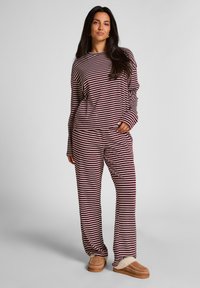 Gestreept loungewear-set in bordeauxrood en crème, met een losse lange mouw top en bijpassende broek. Zacht materiaal met een relaxte pasvorm.