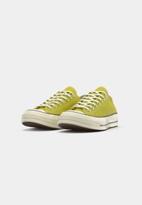 Tenisi verzi din pânză cu șireturi albe, vârf rotund, talpă din cauciuc și un mijloc texturat. Design clasic de tip low-top cu detalii minime.