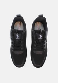 Fekete sportcipők hálós felsőrésszel, vastag gumitalppal és fűzőkkel. A felületen logó és finom textúraváltozások találhatóak.