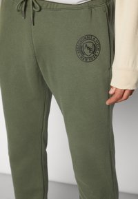 Olivgrüne Jogginghose aus weichem Material mit Tunnelzug am Bund und einem schwarzen, bestickten Logo mit der Aufschrift "Abercrombie & Fitch, New York."