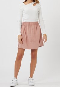 Jupe plissée rose légère avec ceinture élastique. Associée à un haut blanc à manches longues avec une découpe ronde à l'épaule.