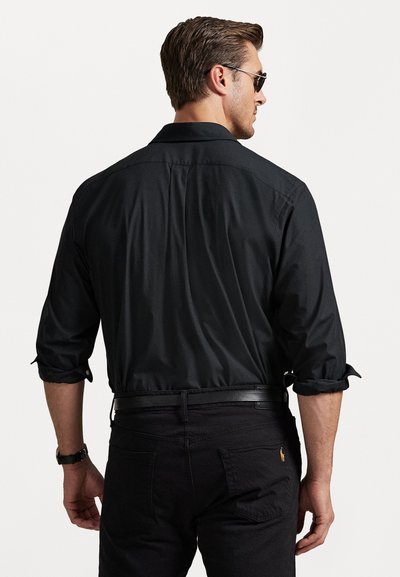 Svart skjorte med oppbrettede ermer, teksturert stoff og rett snitt. Båret med mørke jeans og et svart belte.