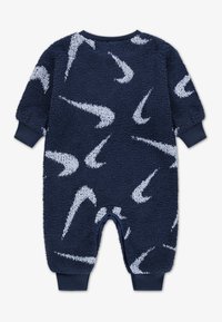 Mono de forro polar azul marino con patrón de Swoosh blanco, puños acanalados, escote redondo y cierre de broches en la parte inferior. Tela suave y texturizada.