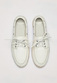 Weiße Lederschuhe mit abgerundetem Zehenbereich, fünf Ösen für Schnürsenkel und einer genähten Jutegummisohle. Markenname innen sichtbar.