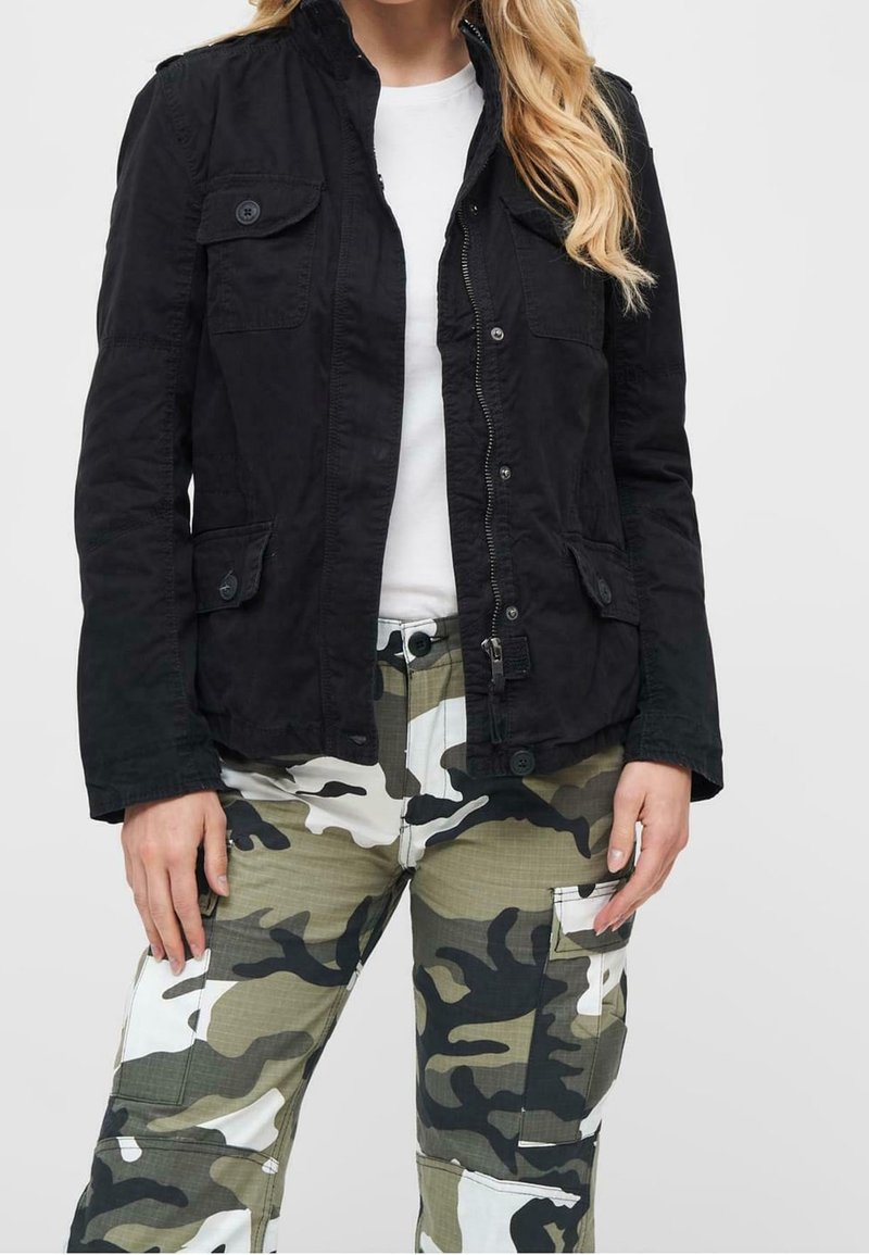 Giacca leggera nera con colletto alto, tasche frontali e chiusure a bottone, abbinata a pantaloni cargo mimetici con più tasche.