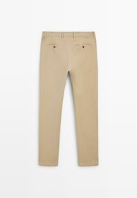 Pantalon beige ajusté vu de dos avec passants de ceinture et deux poches passepoilées boutonnées.
