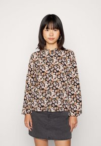 Blusa de manga longa floral em preto com padrões em rosa, branco e castanho. Apresenta um decote alto e pregas no peito. Textura de tecido suave.