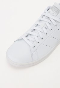 Hvide adidas Stan Smith sneakers med læderoverdel, klassisk snørebåndslukning, perforerede sideløsninger og gummisål.