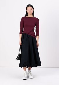 Burgundy figurerad topp med trekvartslånga ärmar, kombinerad med en svart, voluminös midiklänning och vita sneakers. Liten svart handväska.