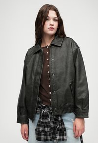 Czarna kurtka z imitacji skóry o luźnym kroju, z zatrzaskami, kieszeniami po bokach i ściągaczem u dołu. Zestawiona z brązową bluzką i flanelą w kratę.