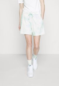 Světle zelené tie-dye šortky s elastickým pasem a šňůrkou, s bočními kapsami a malým logem na přední straně. V kombinaci s bílými teniskami.