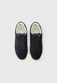 Pantofi slip-on de culoare bleumarin, din suede, cu panouri laterale elastice și o talpă din cauciuc alb. Logo-ul este prezent pe tălpile interioare și pe laterale.