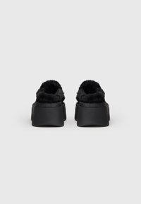 Sorte slip-on sko med en tekstureret overflade og blød indvendig foring. Rund bagende og flad sål for komfort. Ingen synlige detaljer eller beklædning.