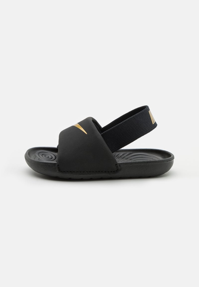 Schwarze Sandalen mit einem breiten Riemen und einem elastischen Fersenriemen. Sie verfügen über einen goldenen Akzent und eine strukturierte schwarze Sohle mit einem kreisförmigen Muster.