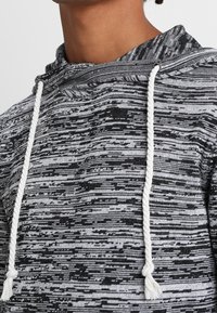 Kapuzensweatshirt mit einem schwarz-weiß gestreiften Muster, gefertigt aus einer strukturierten Stoffqualität und mit kontrastierenden weißen Kordeln.