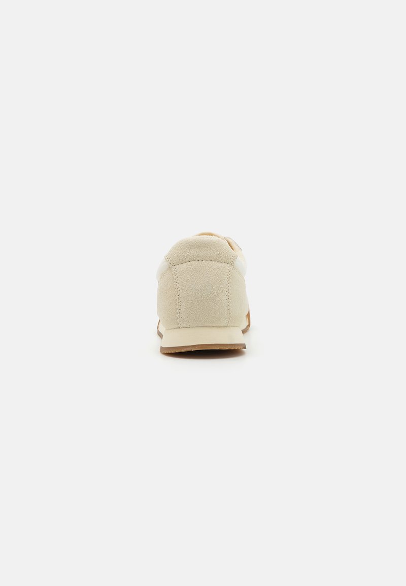 Beige Wildleder-Sneaker mit abgerundetem Rücken, weißen Akzenten und einer strukturierten Sohle. Einfaches Design, keine sichtbaren Logos oder Muster.