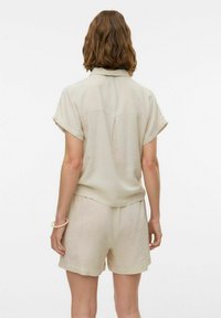 Lys beige linned kortærmet skjorte med en rygfold og matchende shorts. Stoffet har en subtil tekstur, der giver en afslappet, casual pasform.