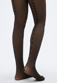 Καλσόν με μαύρα σχέδια καρδιών και διαφανές φινίρισμα, με μια σειρά από μικρές καρδιές κατά μήκος των εξωτερικών πλαϊνών κάθε ποδιού.