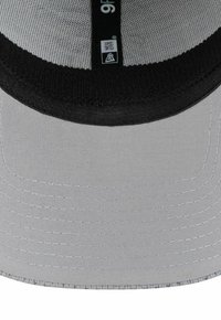 Gros plan sur la partie inférieure d'une casquette snapback New Era 9FIFTY grise et noire, incluant le bord et la doublure intérieure.