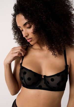 Soutien-gorge en maille noire avec motif à pois, sans armature, bretelles ajustables, nœuds décoratifs aux bretelles et texture transparente.