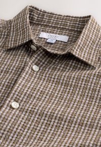 Camisa con cuadros marrones y blancos hecha de tela con textura suave, que cuenta con un cuello puntiagudo y tres botones blancos en la parte delantera.