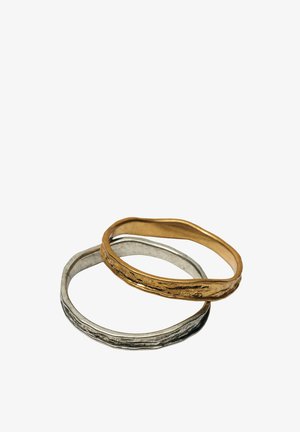 Twee getextureerde metalen ringen, één gouden en één zilveren, die elkaar overlappen op een witte achtergrond.