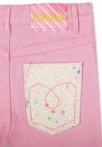 Różowe dżinsy z błyszczącą kieszenią pokrytą brokatem w kształcie serca, wykończoną różową nitką oraz markową metką w pasie.