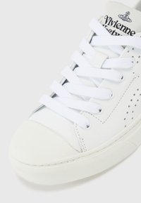 Λευκό δερμάτινο sneaker με περφορέ πικες λεπτομέρειες, επίπεδες λευκές κορδόνες και υφασμένο καουτσούκ σόλα. Διαθέτει στρογγυλή μύτη και λογότυπο στο ταμπελάκι.