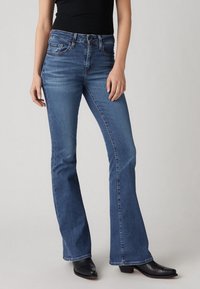 Sinised ekslevad teksad teksakangast, millel on keskmise kõrgusega vöökoht, viis taskut ja õrn pleekimine, sobitatud mustade kontsaga saapadega.