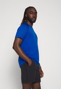 Blaues T-Shirt mit kurzen Ärmeln, strukturiertem Muster und rundem Ausschnitt, kombiniert mit schwarzen Shorts mit Seitentaschen und einem schlichten Design.