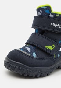 Stivale per bambini blu navy con superficie testurizzata, caratterizzato da motivi verdi e blu, doppie cinghie in Velcro e una suola robusta per una buona trazione.