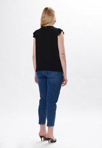 Sort ærmeløs top med teksturerede polka dot-mønstre, flæse-skulderdetaljer, parret med mid-rise blå denim jeans og sorte hælede mule-sko.