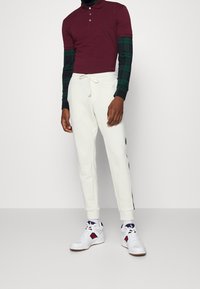 Bordó polo triko s límečkem, dlouhé rukávy v zelené kostkované úpravě, bílé tepláky se šňůrkou a bílé tenisky s námořnickými a červenými akcenty.