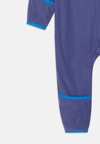 Lila fleecepyjamas med blå detaljer, utrustad med ribbade muddar och en mjuk textur. Designad för komfort och rörelsefrihet.