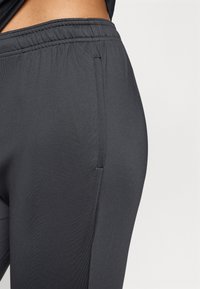 Fekete sportnadrág elasztikus derékkal, sima felülettel és oldalsó varrás részletekkel. Az anyag rugalmas és testhez simuló.