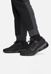Schwarze Sportschuhe mit einem Obermaterial aus Netzgewebe, Gummisohle und auffälliger Dämpfungseinheit, kombiniert mit dunklen, eng zulaufenden Jogginghosen.